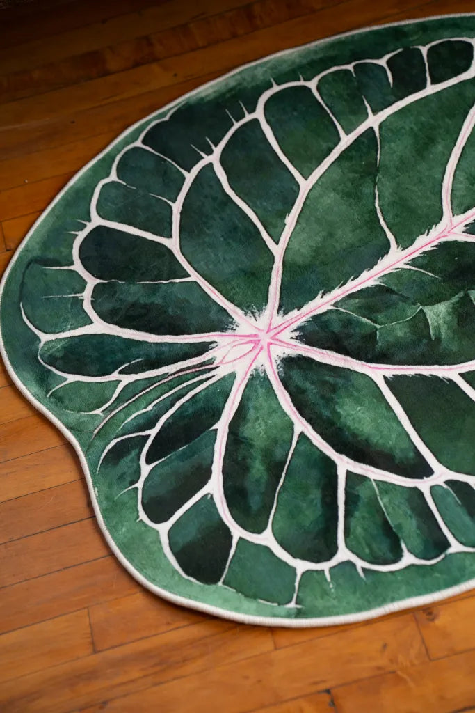 Close-up of leaf rug on wood floor, showing rich green textures and pink vein details in natural lighting.