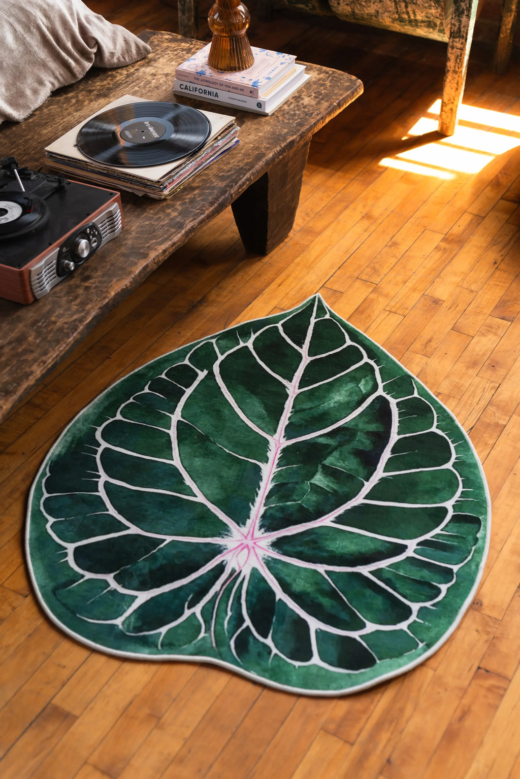 Leaf rug placed beside a rustic table and vintage chair, on sunlit wood floor with warm tones.