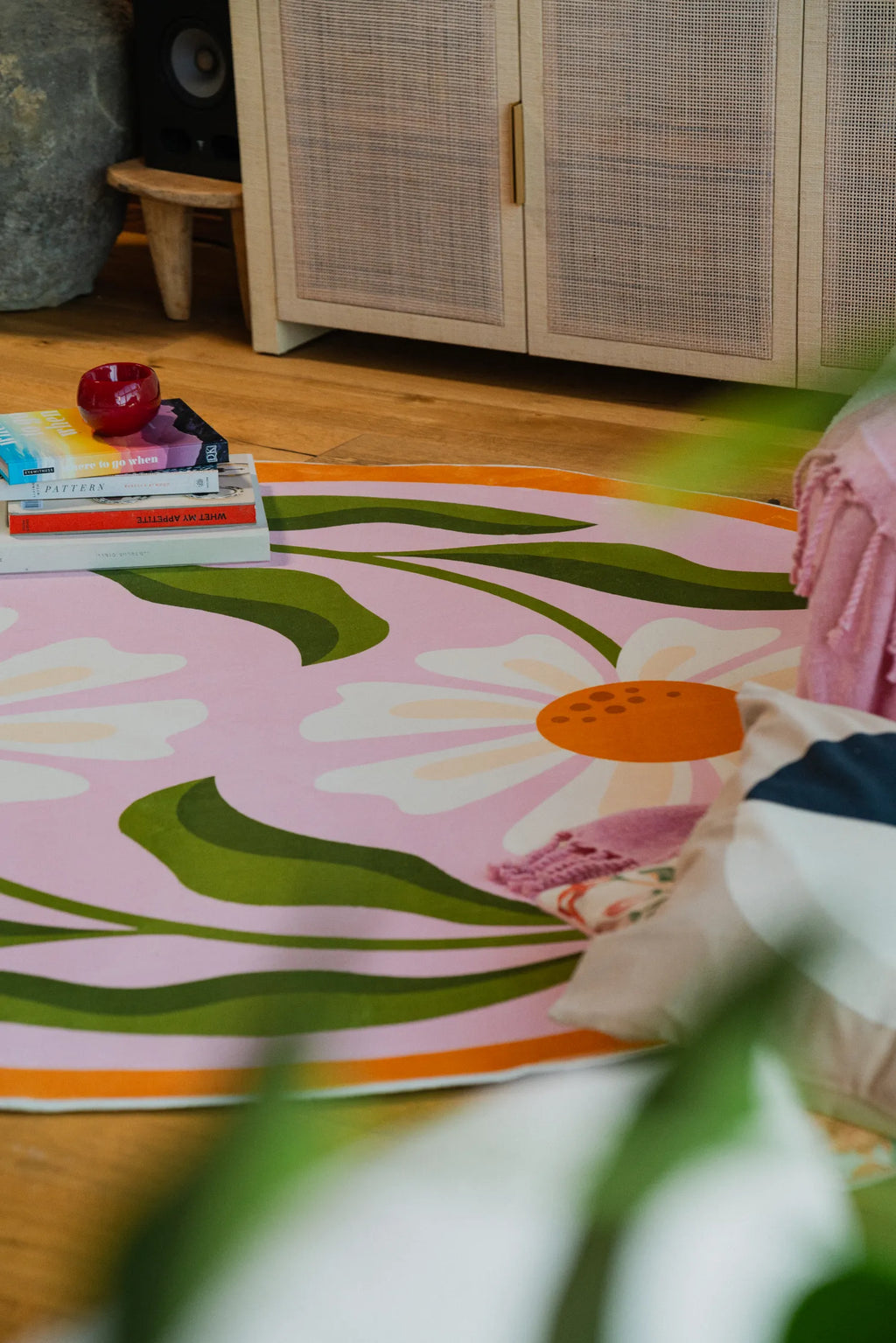 Close-up of the pink daisy rug showing vibrant floral details and books stacked nearby