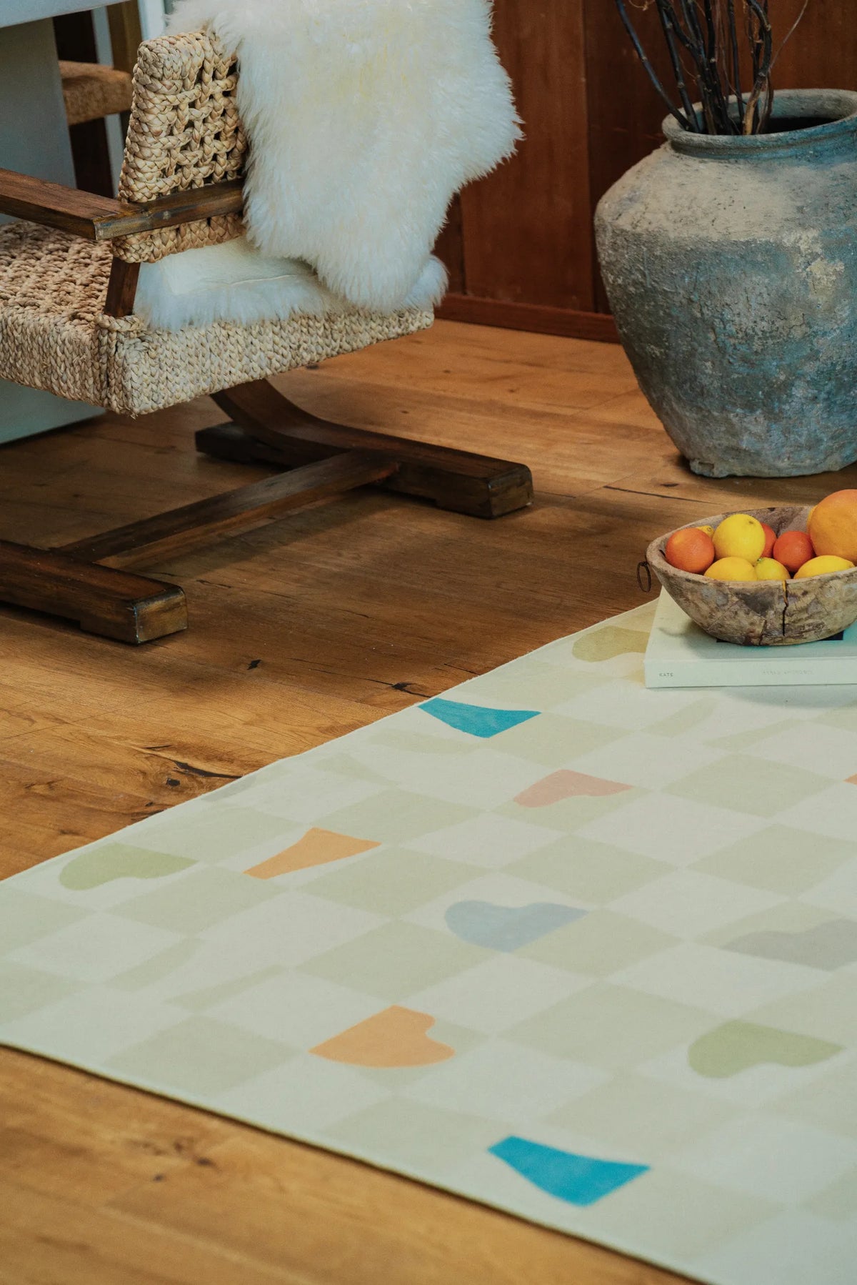 Pale oat pastel rug placed beside a woven rocking chair on rustic plank floor.