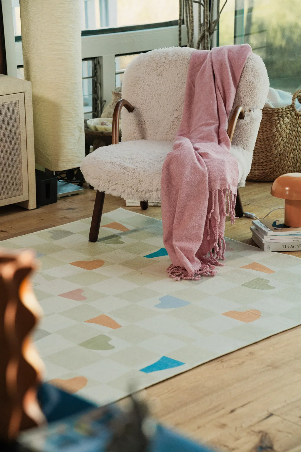 Soft neutral rug grounded beneath a cozy lounge chair in a wood-floored corner, adding a playful rug touch