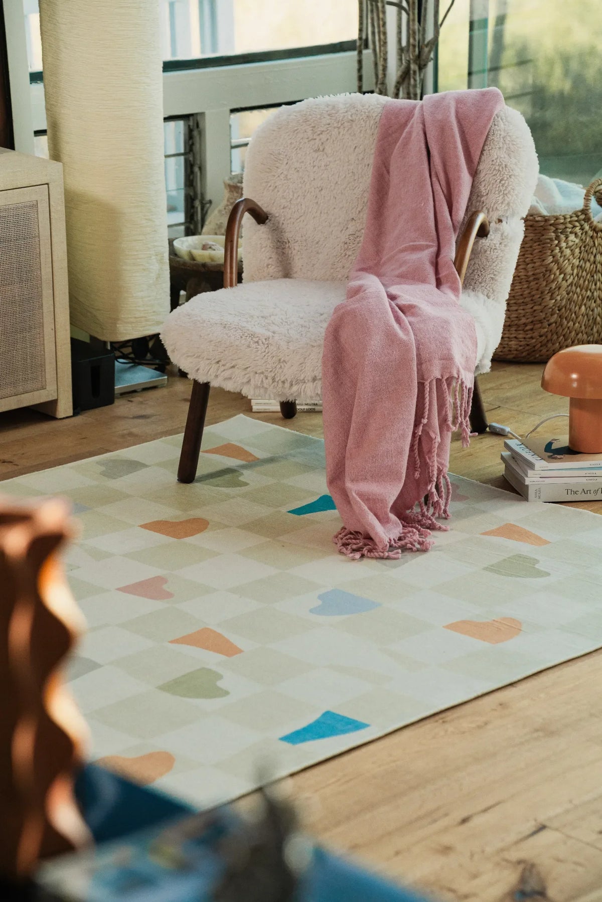 Soft neutral rug grounded beneath a cozy lounge chair in a wood-floored corner, adding a playful rug touch