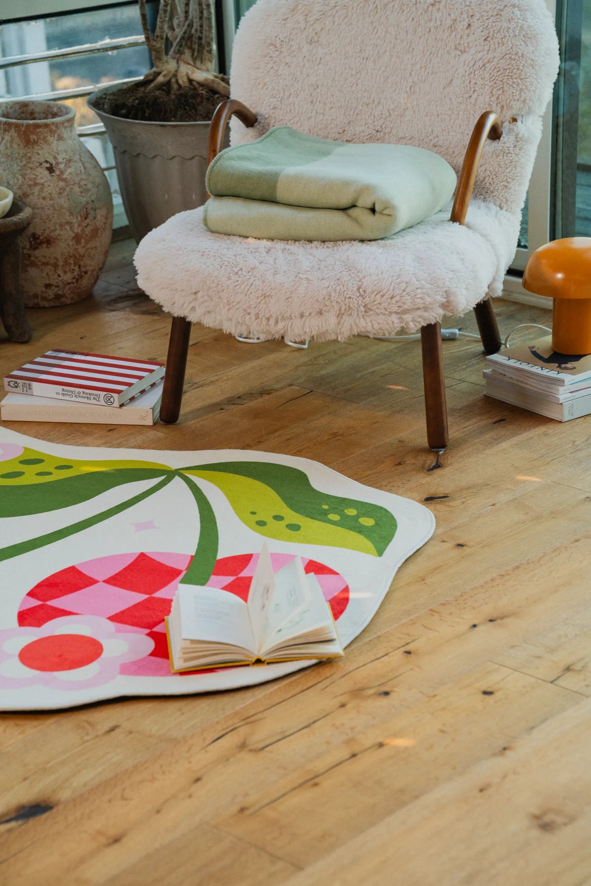 Red and pink cherry rug laid in front of a cushioned chair on sunlit wood floor.