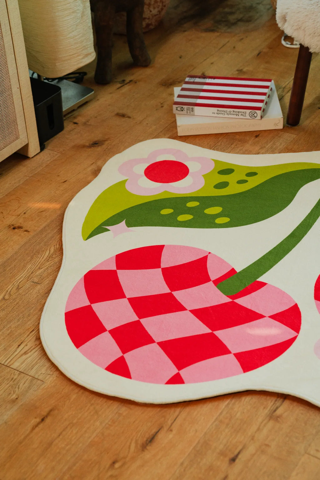 Close-up of the cherry rug’s checkered fruit and curved edge resting on smooth wood floor.