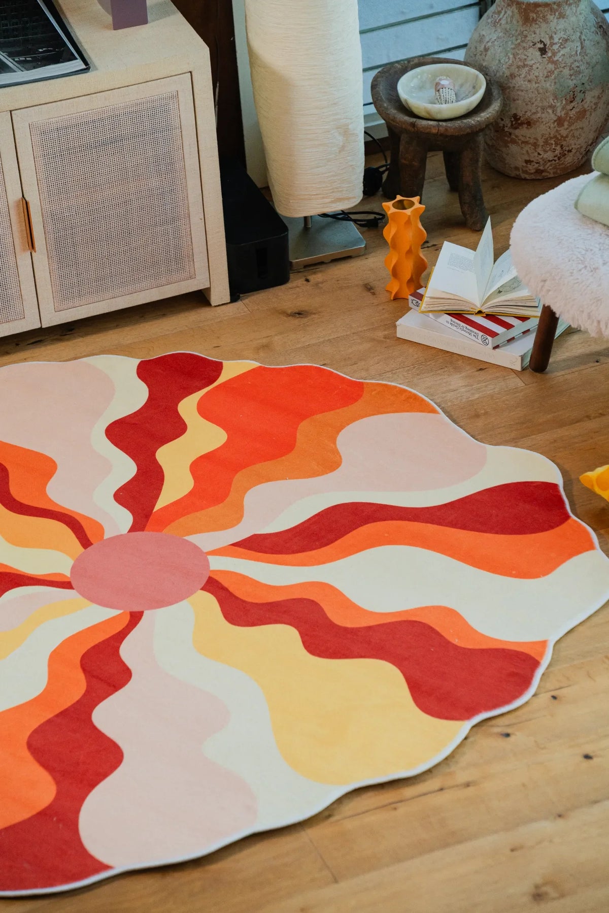 Close-up of the sundial orange rug with wavy sunray patterns, styled in a cozy corner with soft seating and books.