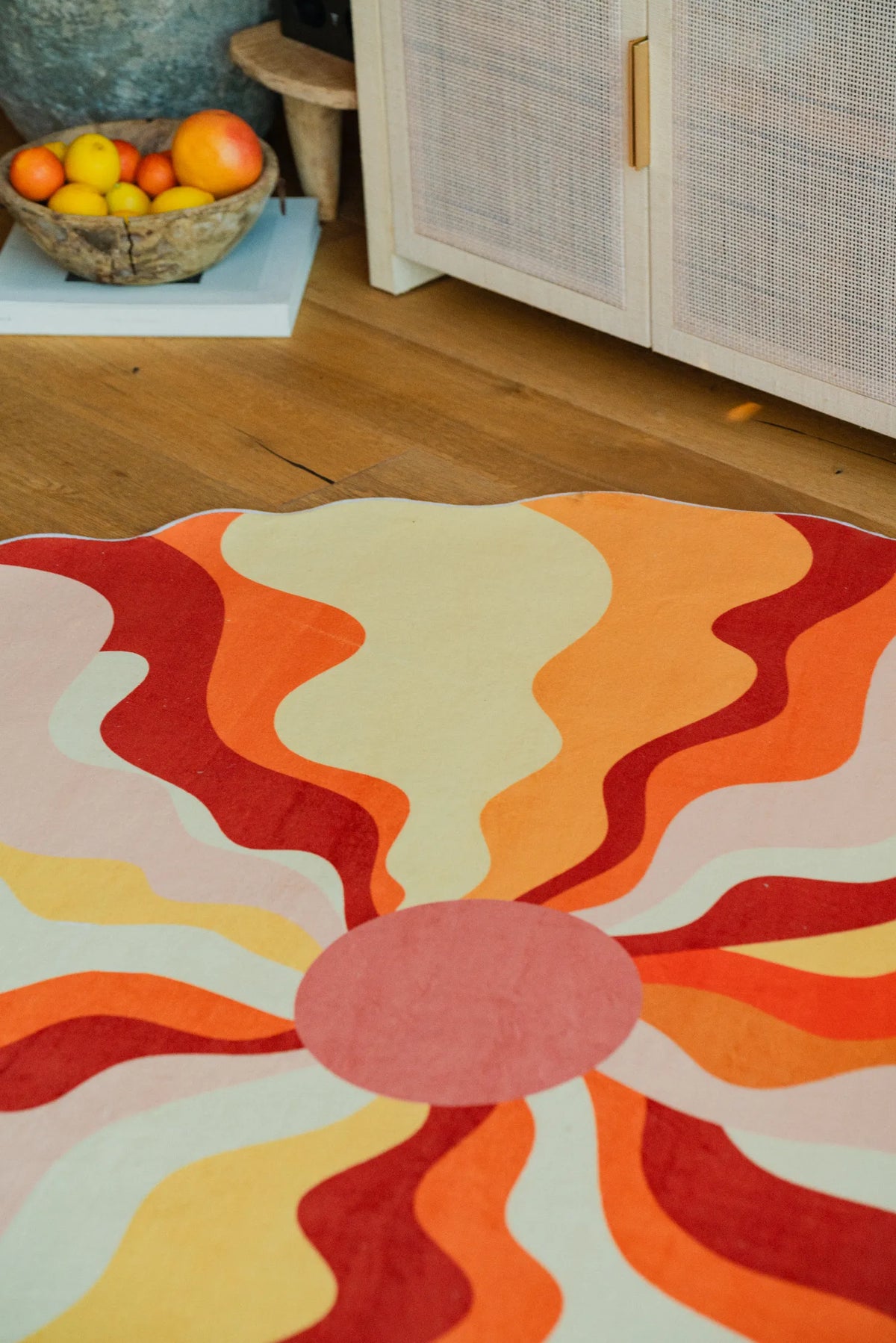 Detail view of the vibrant orange rug's flowing shapes and warm palette, next to a bowl of fresh citrus on the floor.