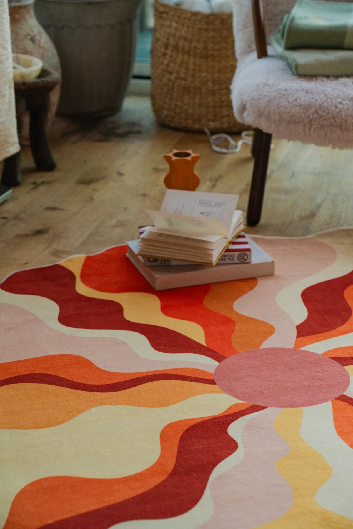 A close-up of the sundial orange rug with books stacked beside a cozy chair in the corner.