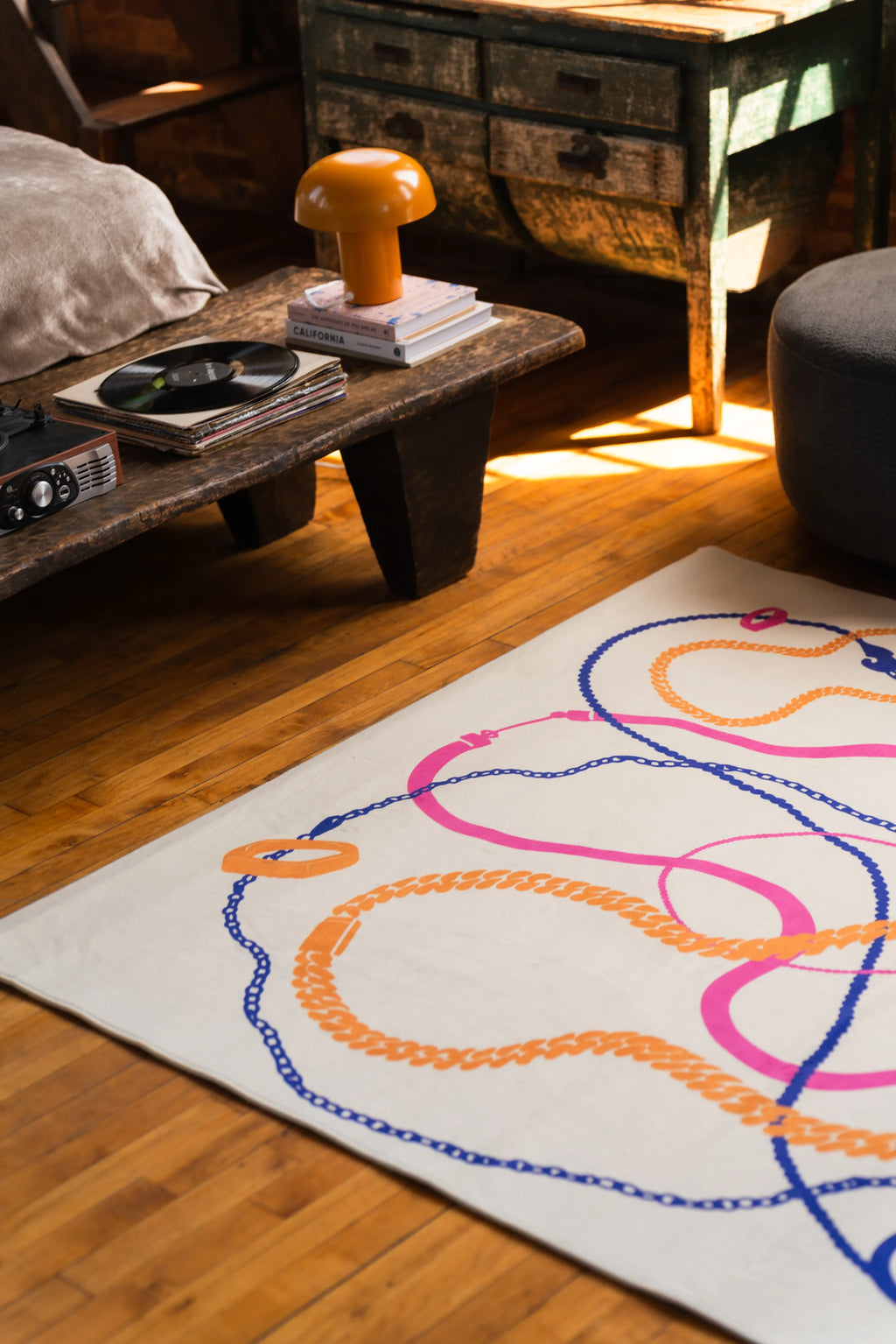 Close-up of a pastel abstract rug on hardwood floor, featuring curved orange, pink, and blue lines next to a rustic table