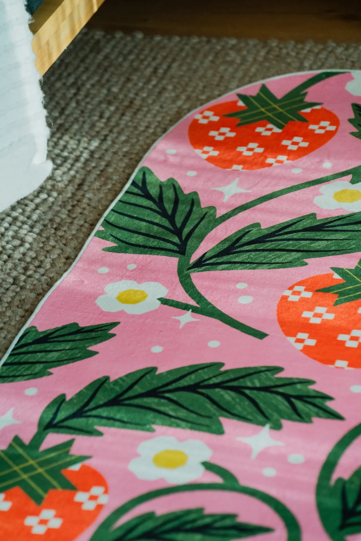 Detail of the pink runner rug showing playful fruit pattern and curved edge on carpeted floor.