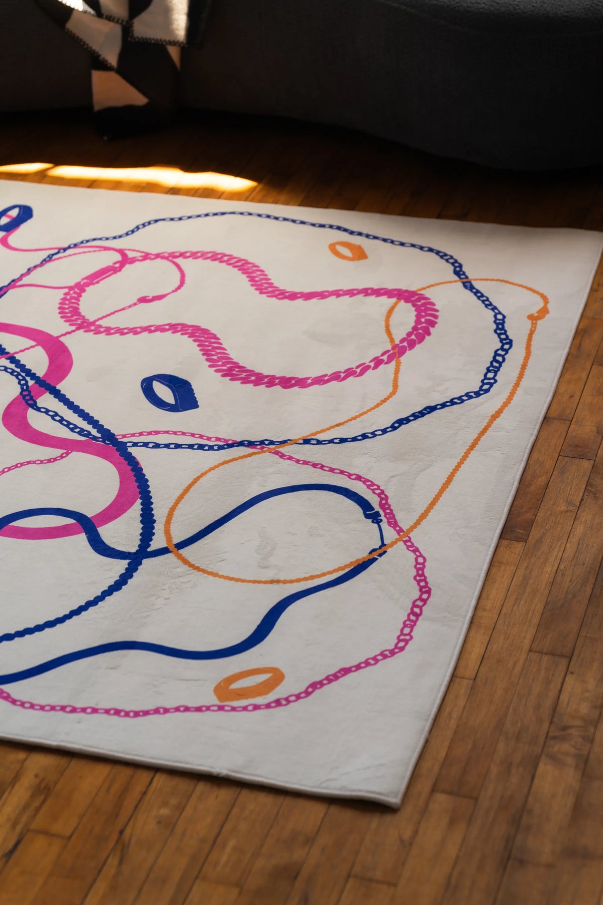Close-up of pastel abstract line rug with orange, pink, and blue curves on cream background near a dark sofa