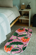 The Sicilian Strawberry Pink Runner Rug by Megan Roy is laid beside a bed on textured carpet floor.