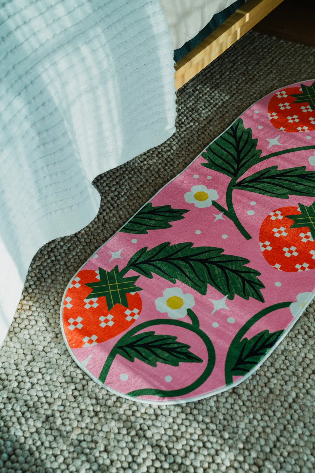Pink runner rug with bold strawberry motifs placed at the bedside over a neutral woven carpet floor.