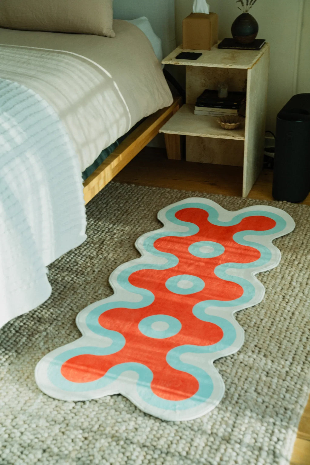 Red coral runner rug with aqua trim laid beside bed on woven beige carpet in cozy bedroom setting.