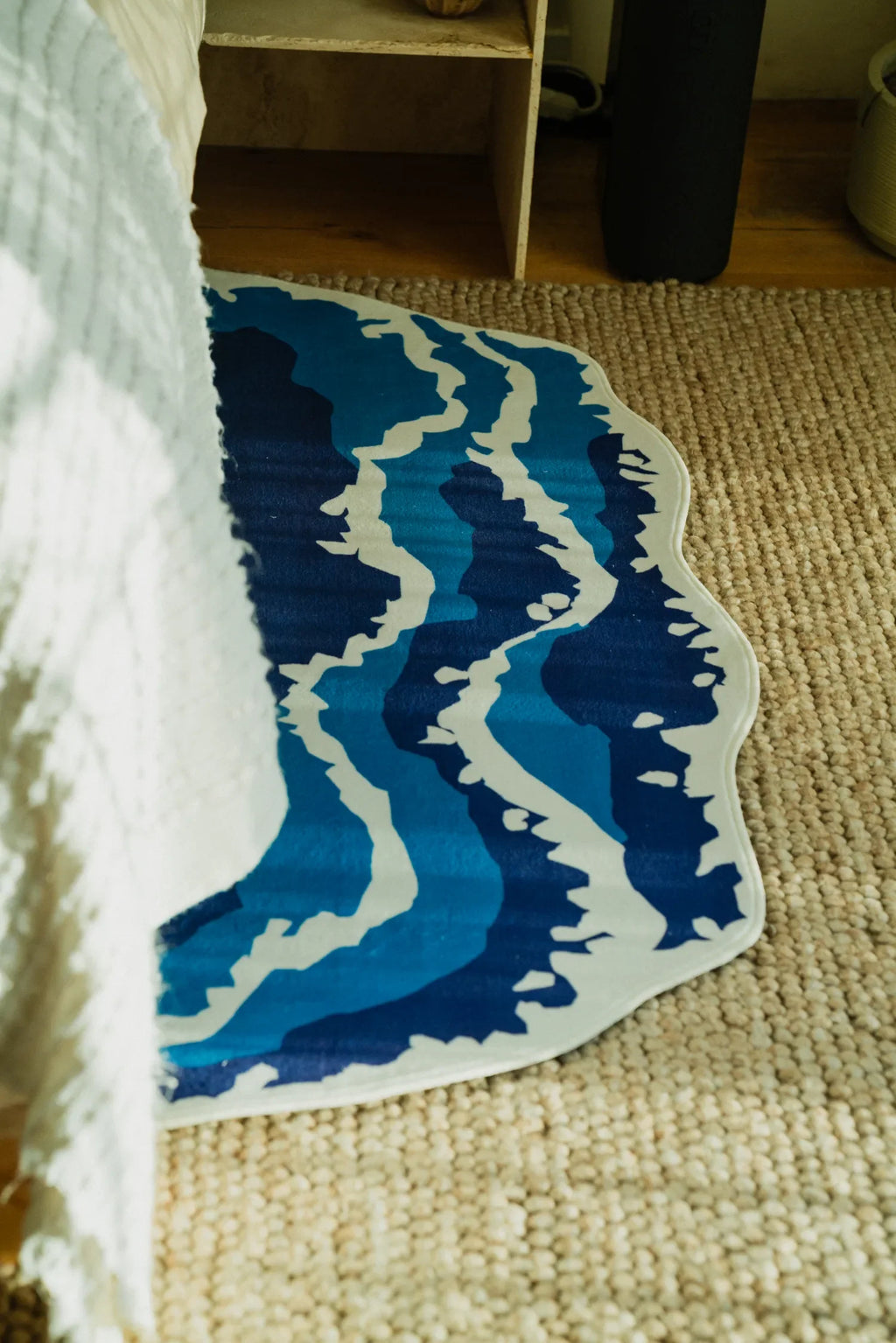Irregular Shaped Blue Wavy Runner Rug placed beside bed on woven carpet for a cozy, textured bedroom look.