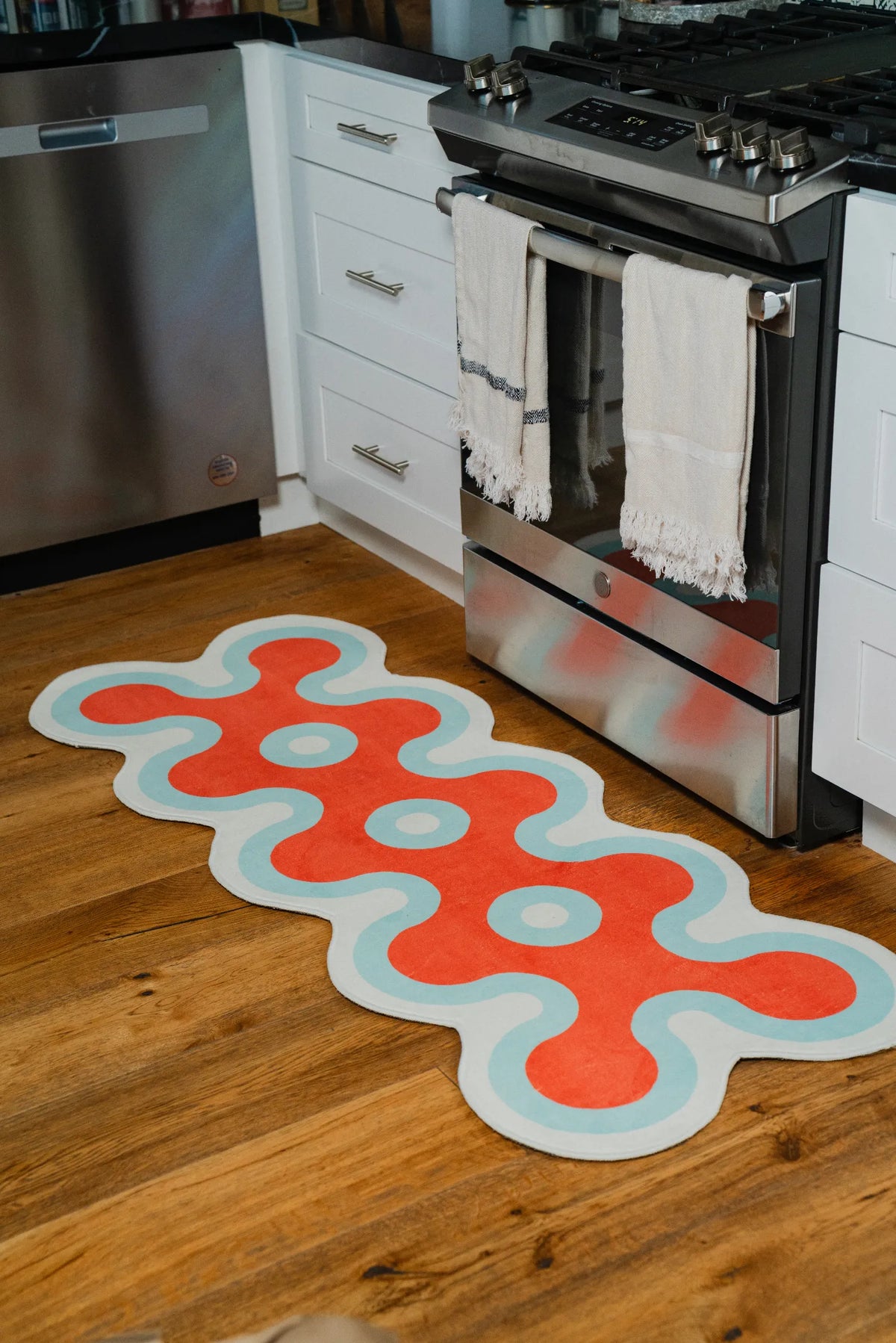 Red coral runner rug with aqua trim placed in front of stove in a modern kitchen with wooden floor.