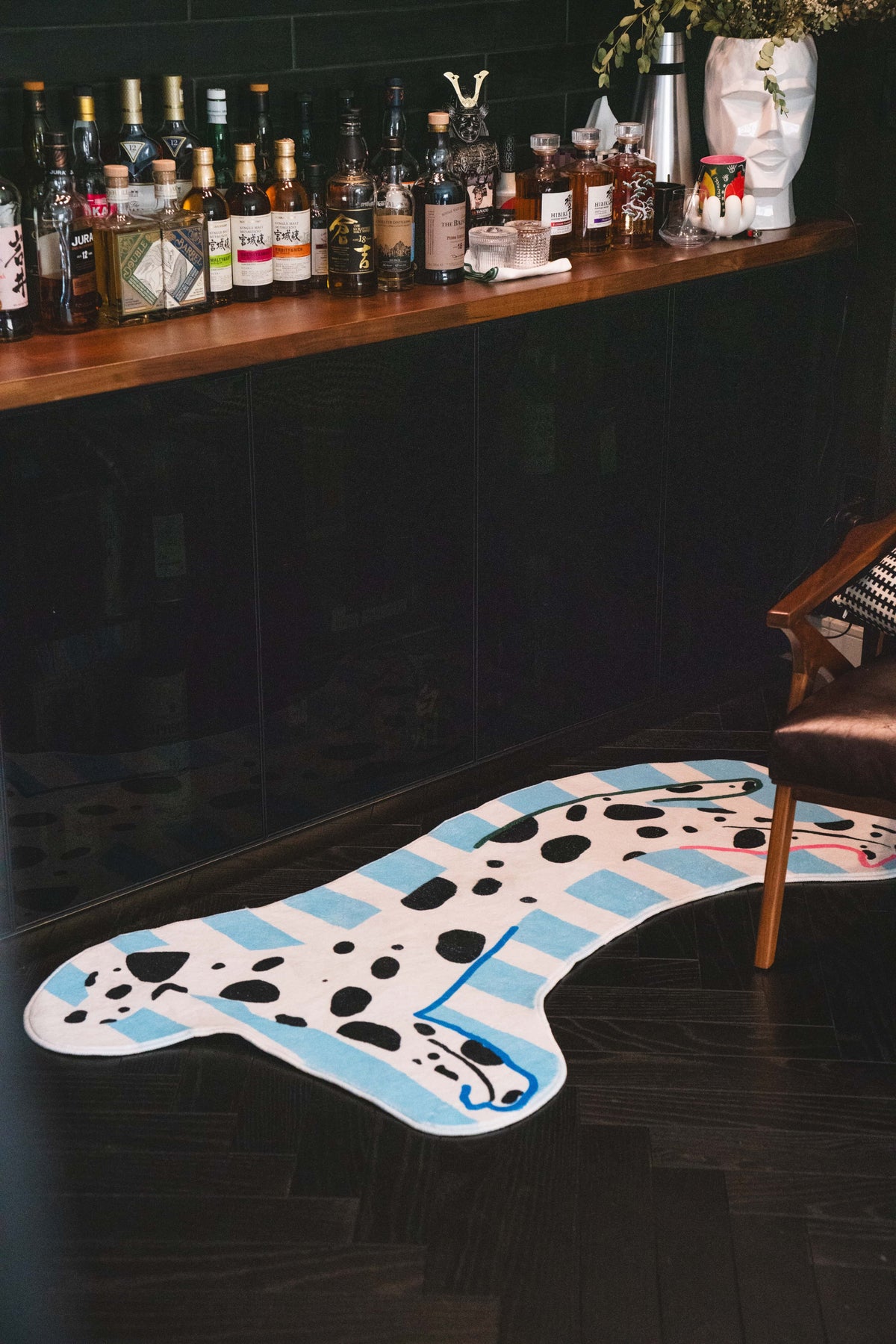 Dog-shaped runner rug placed by a moody bar counter, adding playful contrast next to bottles and a leather armchair.