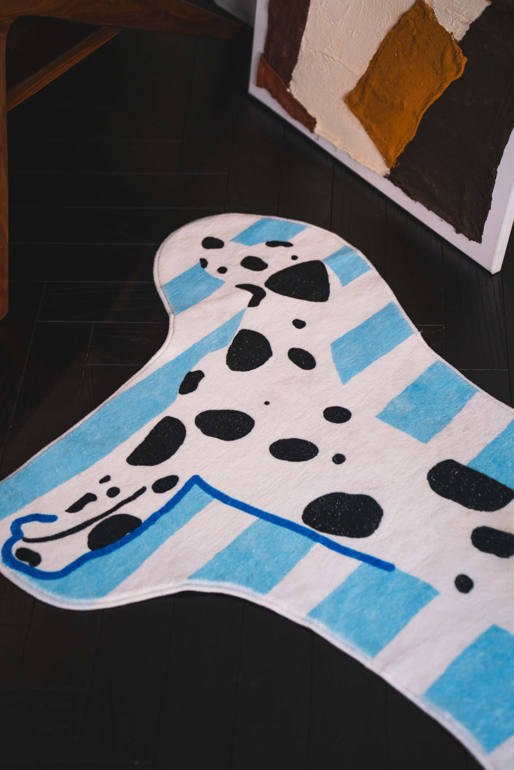Close-up of the dog runner rug showing blue stripes and black spots, styled on dark floor beside leaning abstract artwork.
