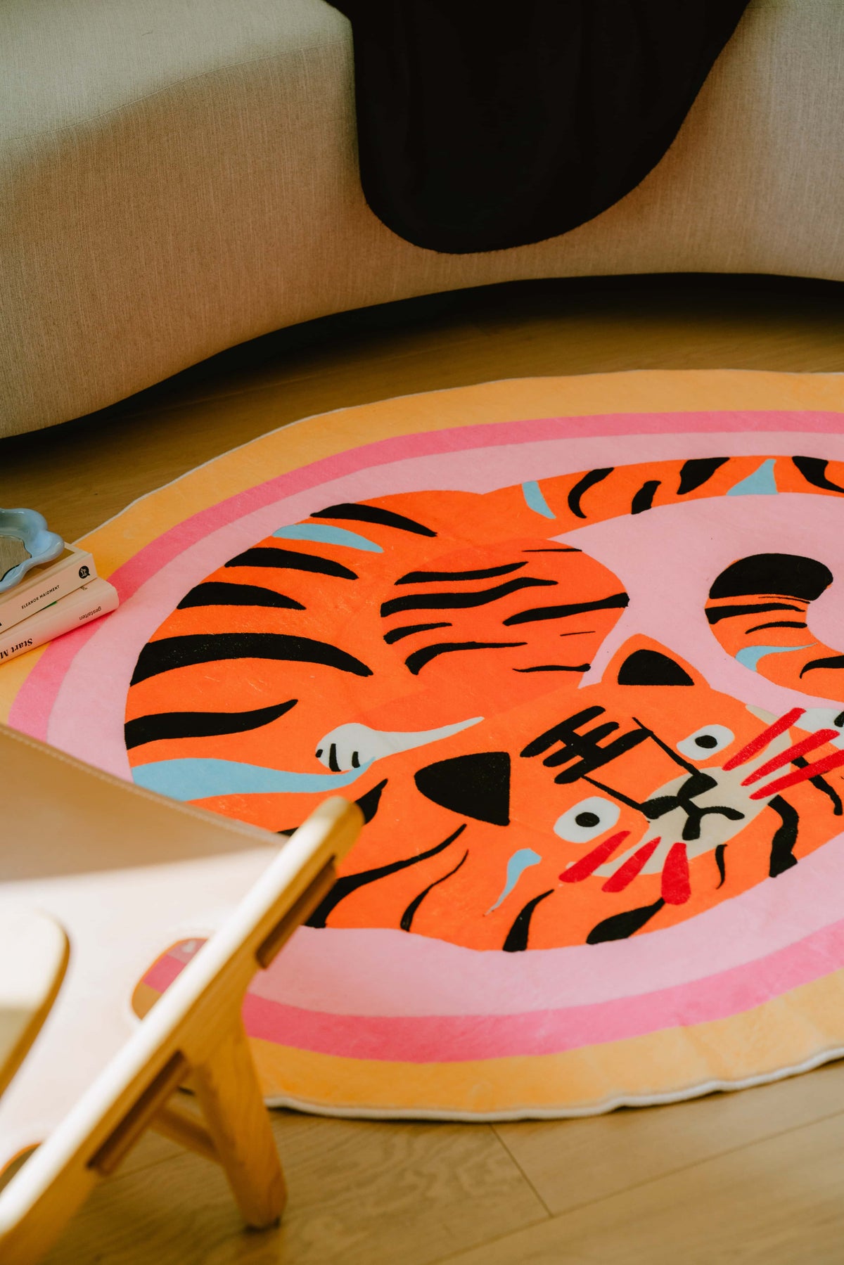 A close-up of the pink tiger rug under a beige sofa, showing vivid stripes and smooth curves in a cozy living area.