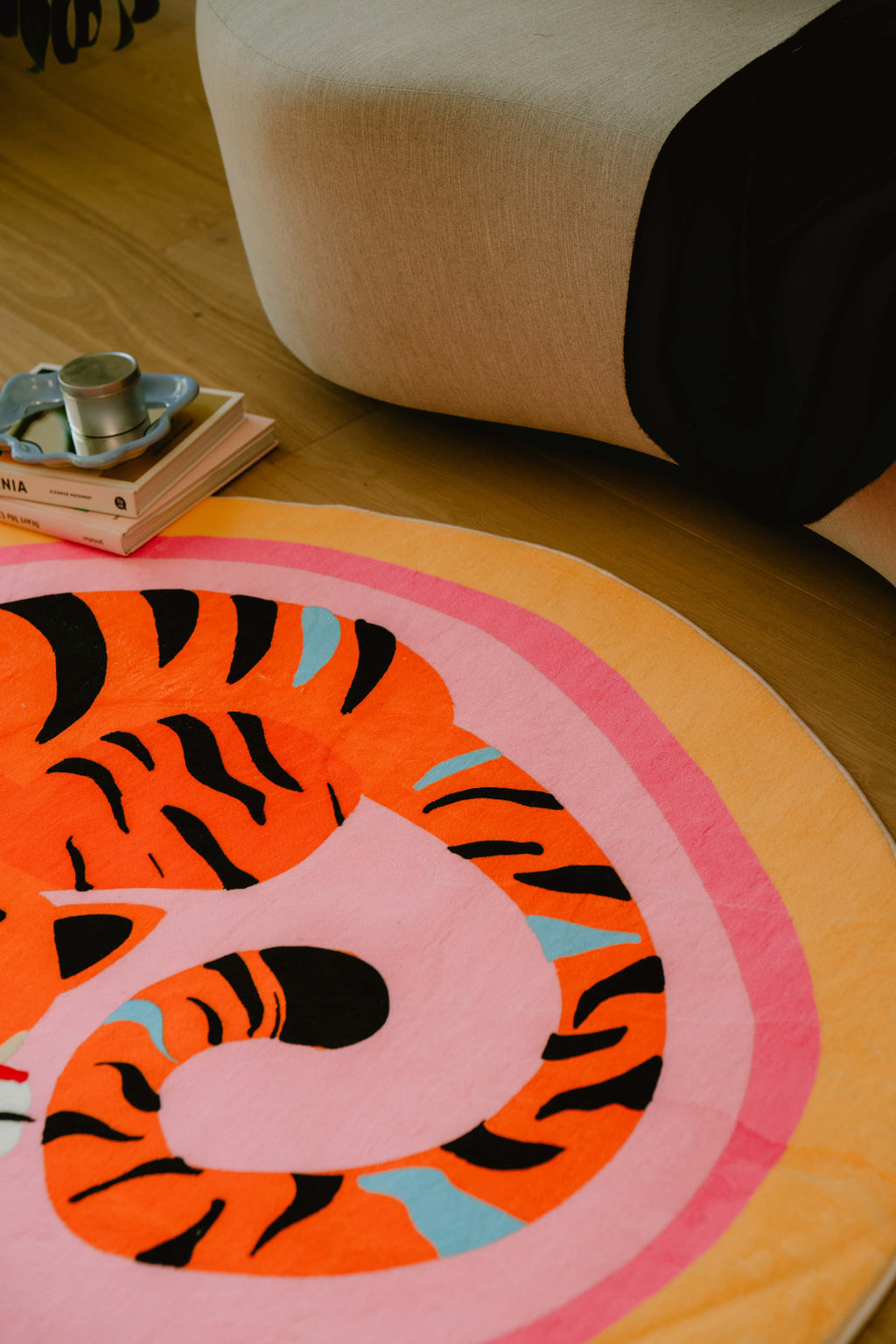 Zoomed-in view of the pink tiger rug’s tail curls near the sofa, with a stack of books and candle tray in the background.