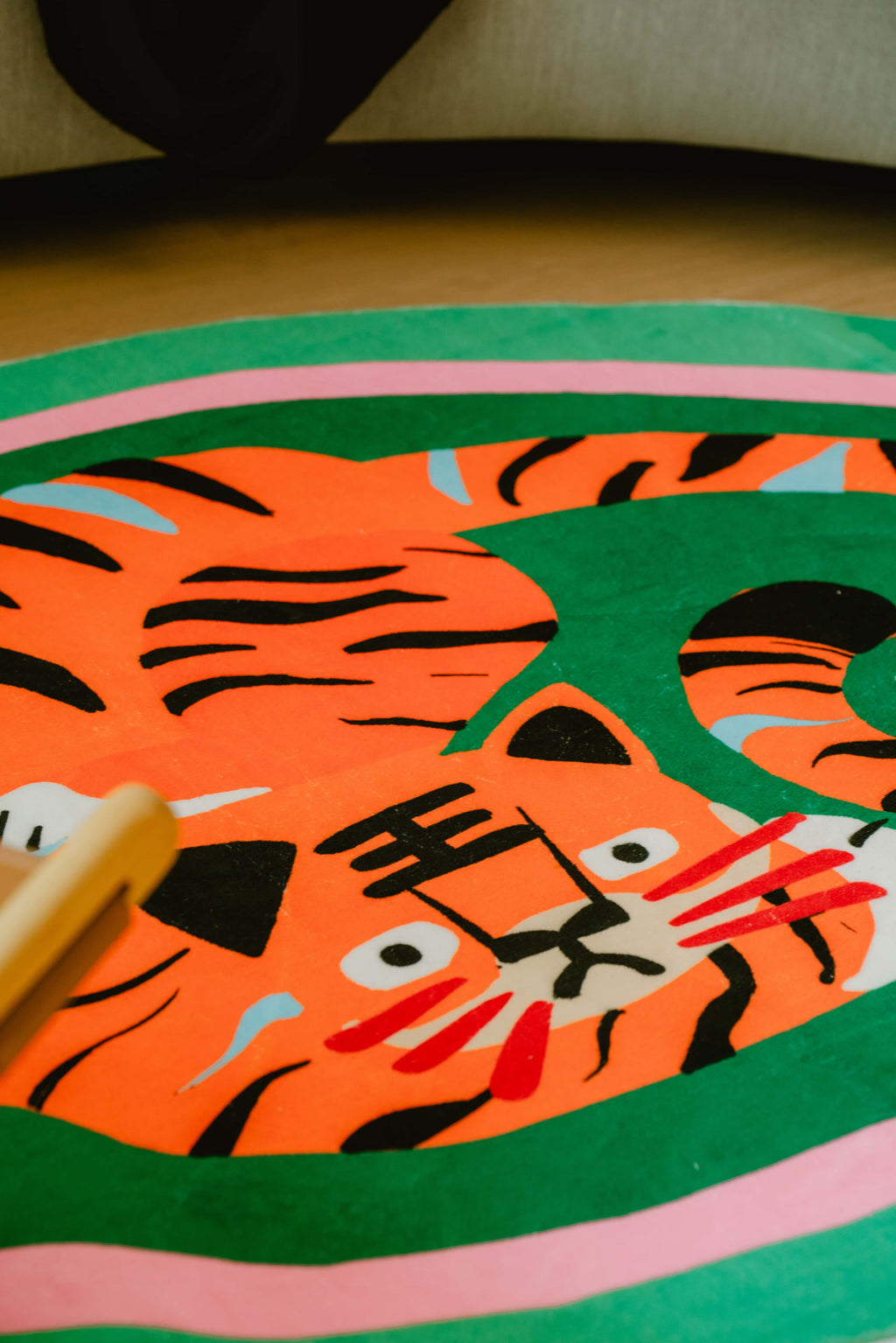 Detail shot of the green tiger rug's head and ears with playful stripes, next to a light wooden chair and soft lighting.
