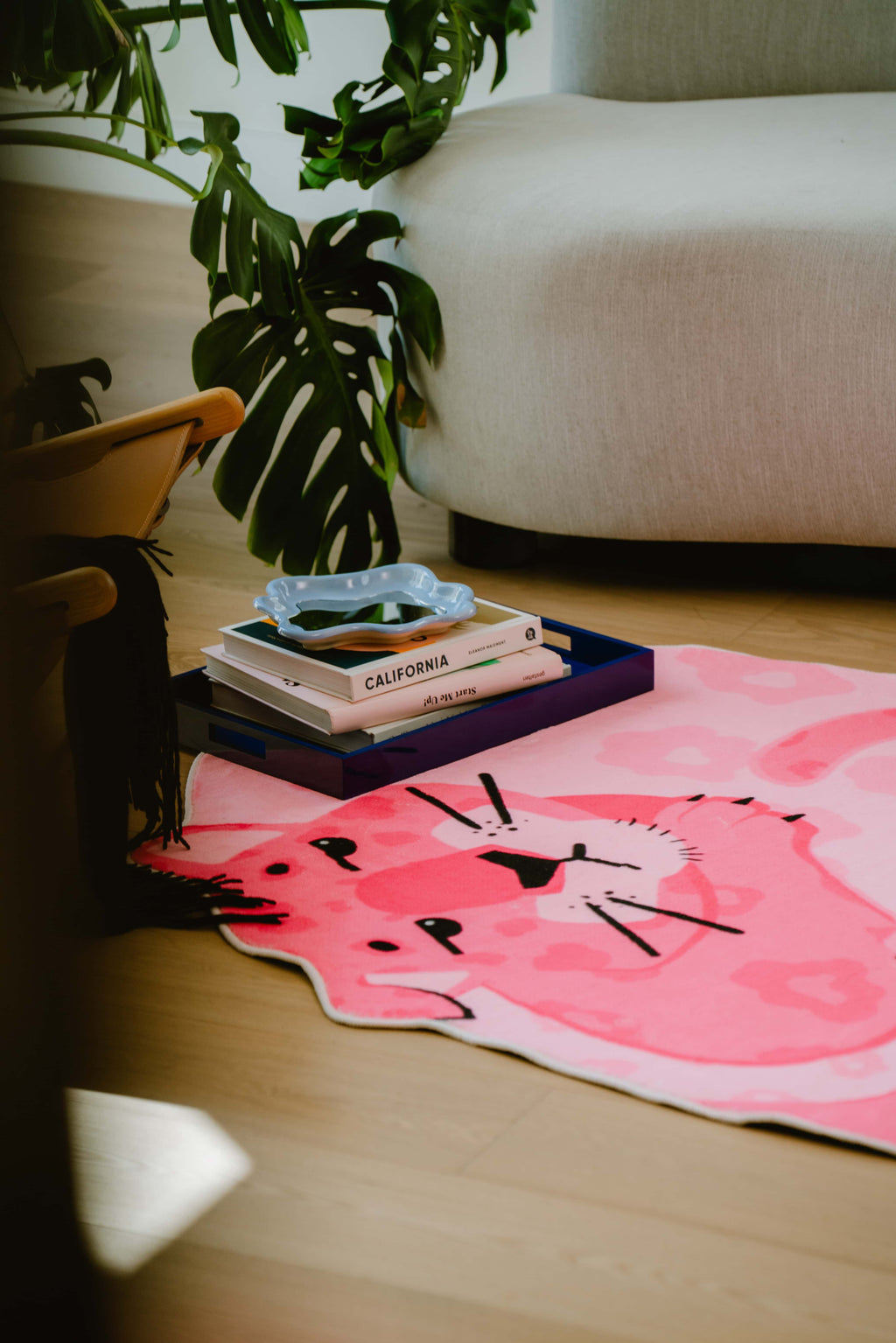 Curved couch and lush plant frame the pink panther rug in a reading nook, showing part of the rug’s head and tail in warm light.