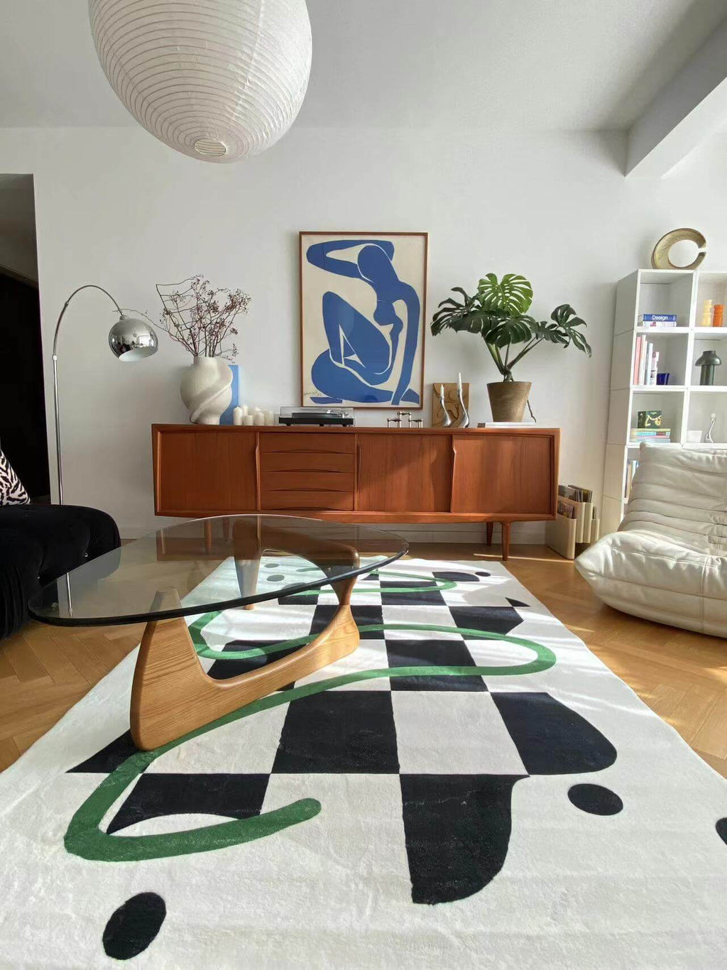 Modern living room with a black and white checkered rug featuring green swirls, paired with a glass coffee table and wood sideboard.
