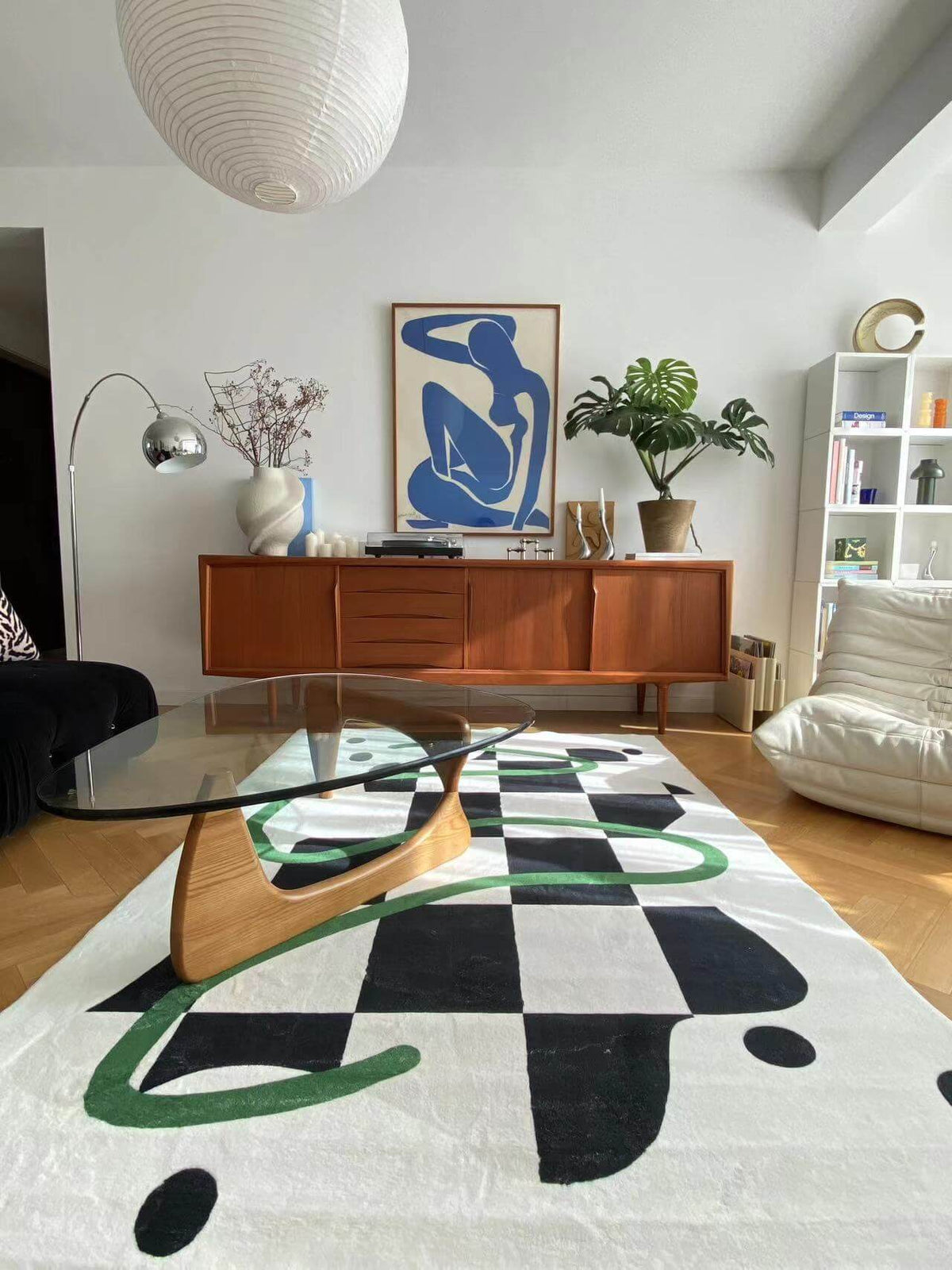 Modern living room with a black and white checkered rug featuring green swirls, paired with a glass coffee table and wood sideboard.