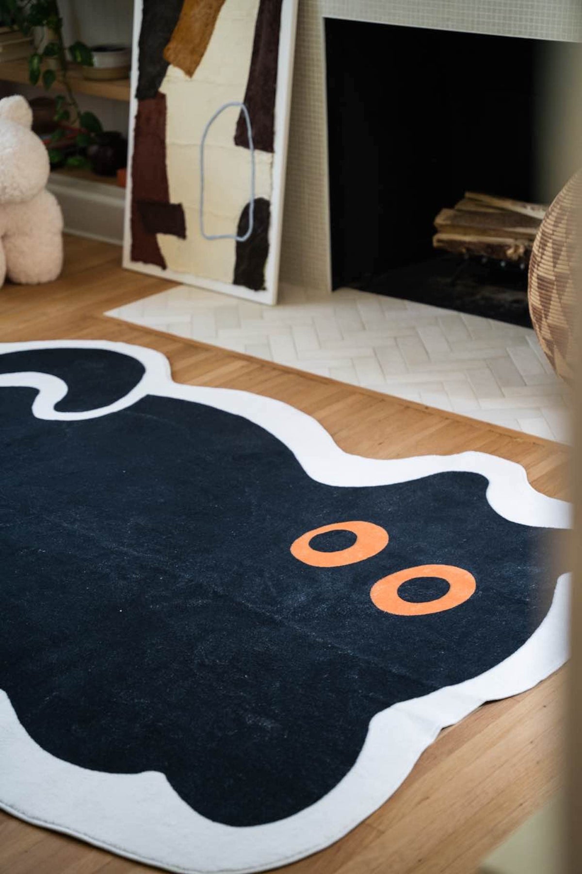Partial view of the black cat rug with bold eyes in front of a modern fireplace and abstract artwork.