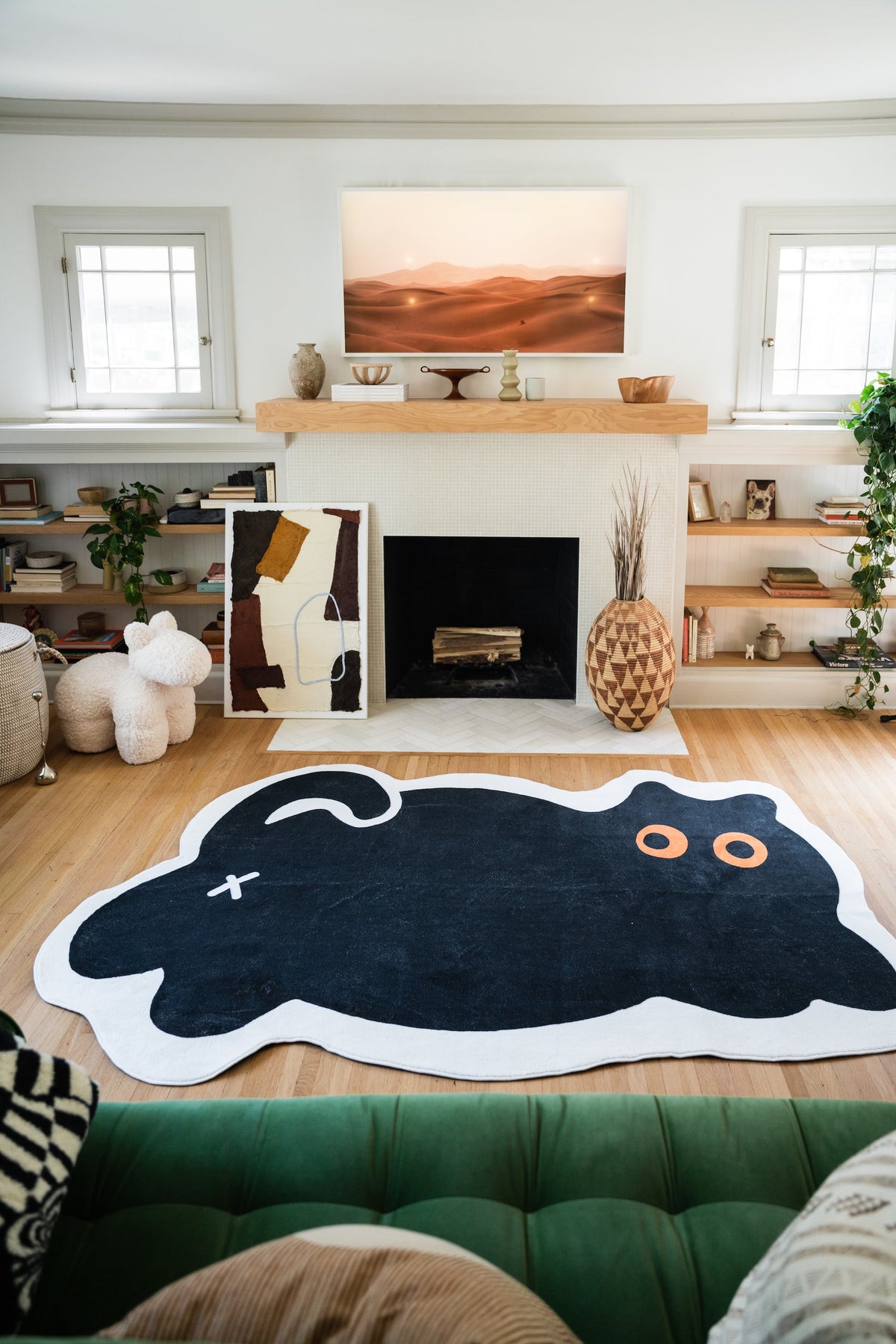 Cute Black Cat Rug laid in a cozy living room with a fireplace and green velvet sofa in the foreground.