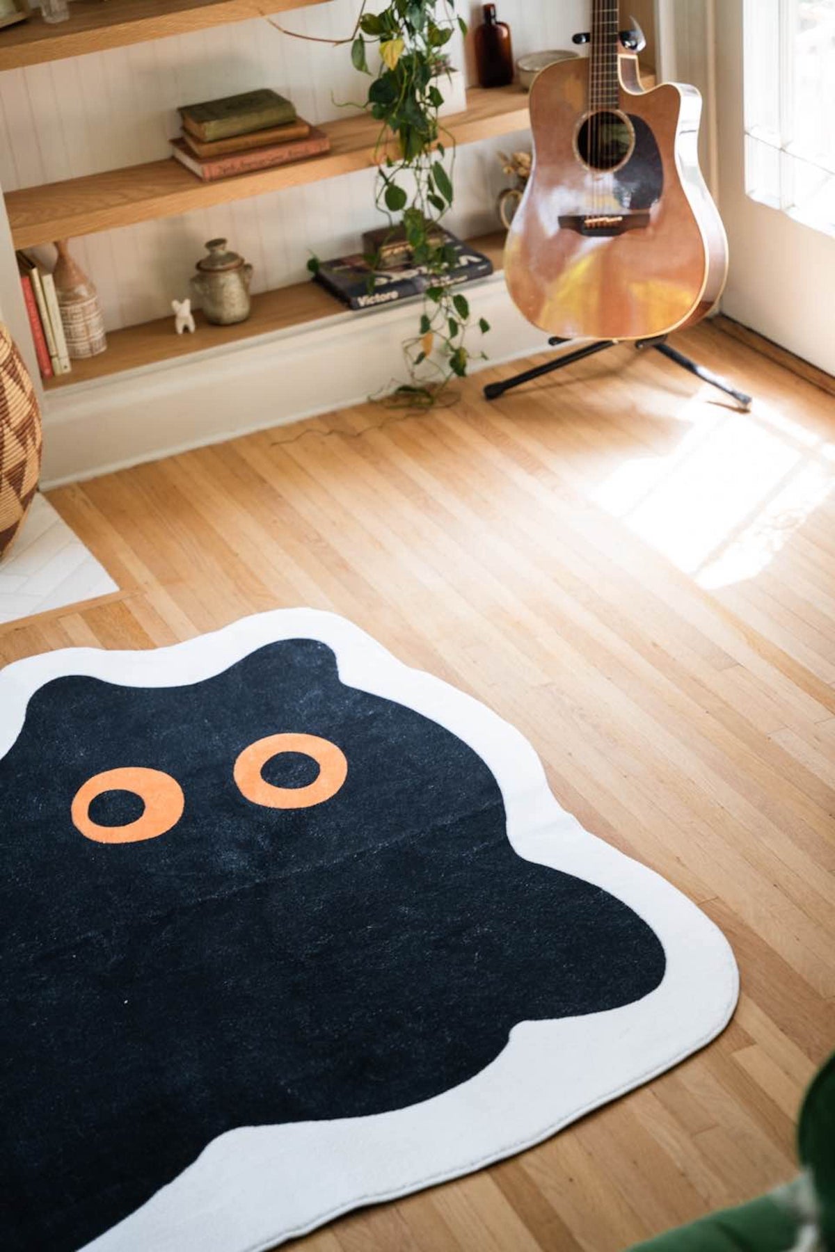 Close-up of the cat-shaped rug’s orange eyes near a guitar and shelf in natural daylight.