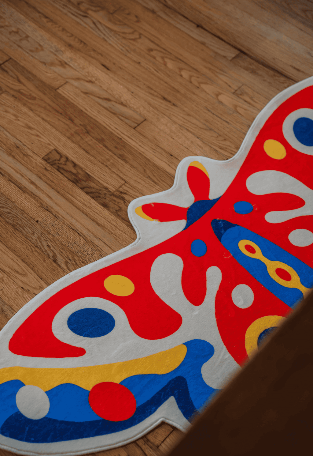 Close-up of butterfly rug on medium-tone wood flooring, showing vivid abstract shapes and plush texture.