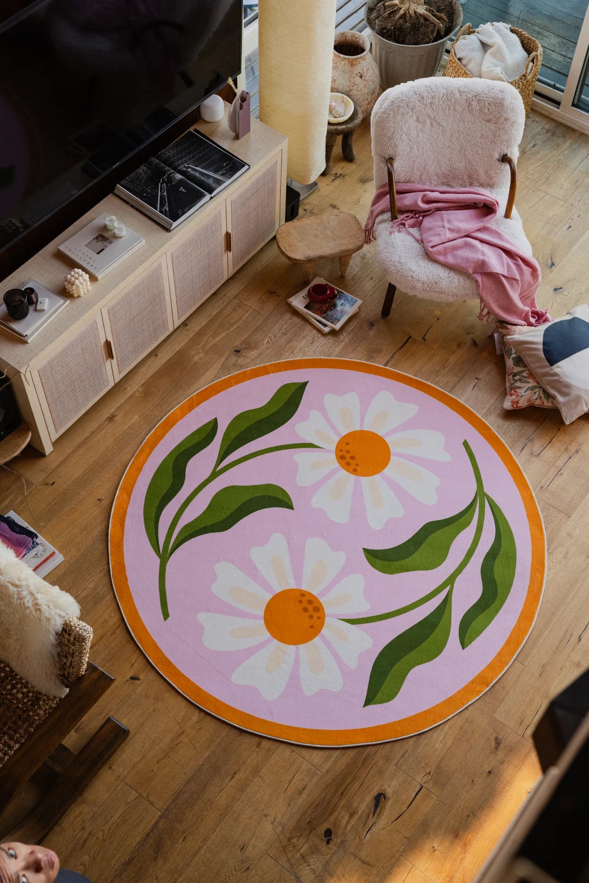 A closer look at the pink daisy rug beside a fluffy armchair and patterned pillows.