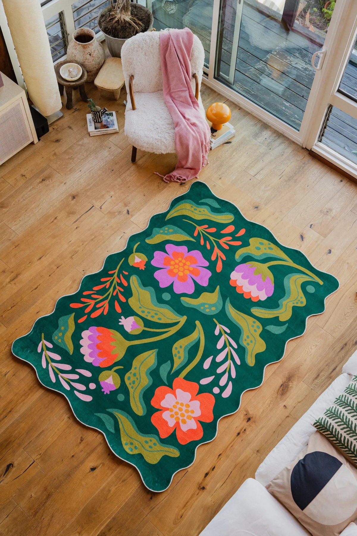 The Green Base Pink Floral Wavy Rug by Jessica Miller, 5' × 7', is styled in a bright living area with wood floor.