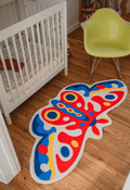 Butterfly rug on warm-toned wood floor beside a white crib and molded chair, in a softly lit corner nook.