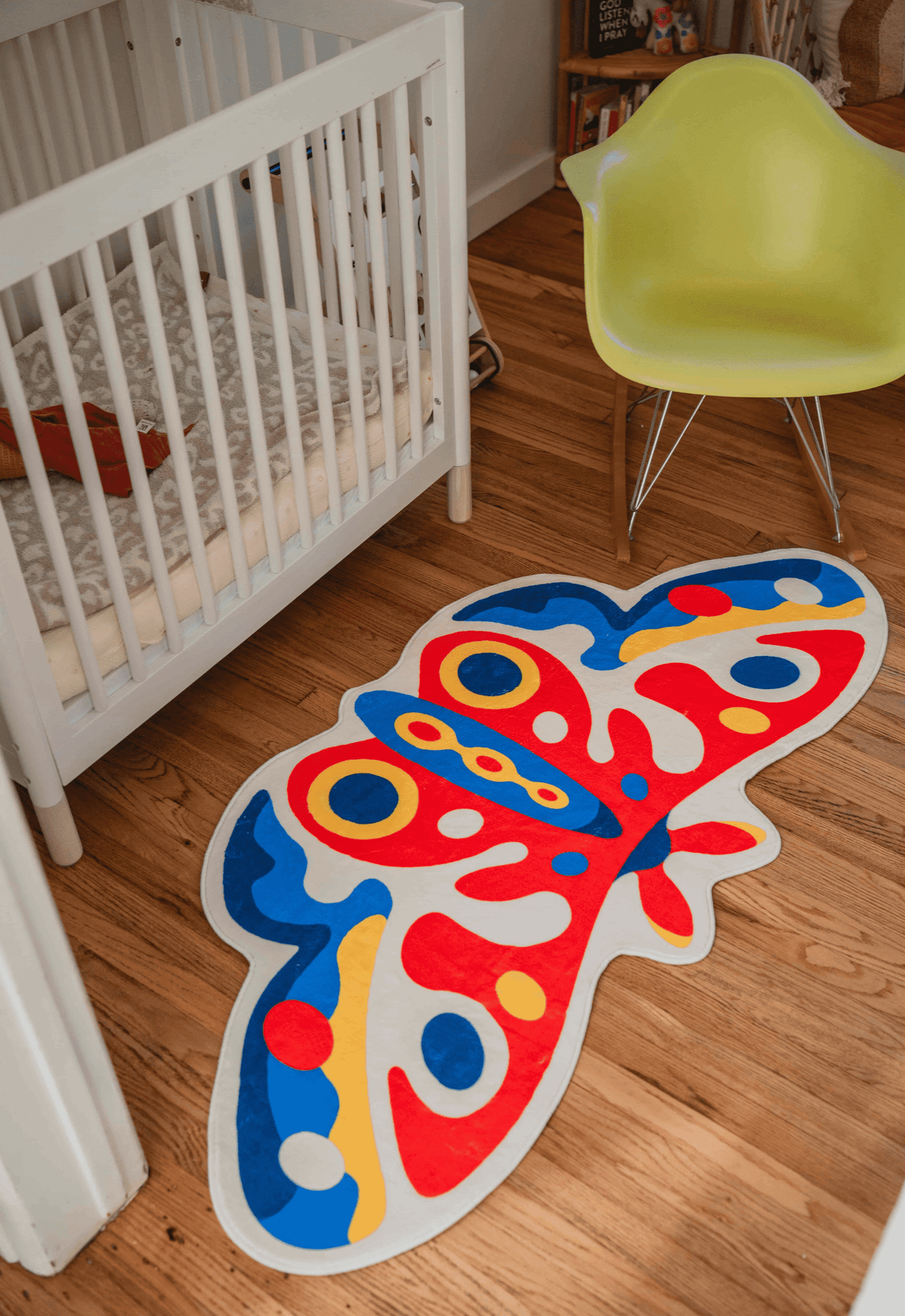 Butterfly rug on warm-toned wood floor beside a white crib and molded chair, in a softly lit corner nook.