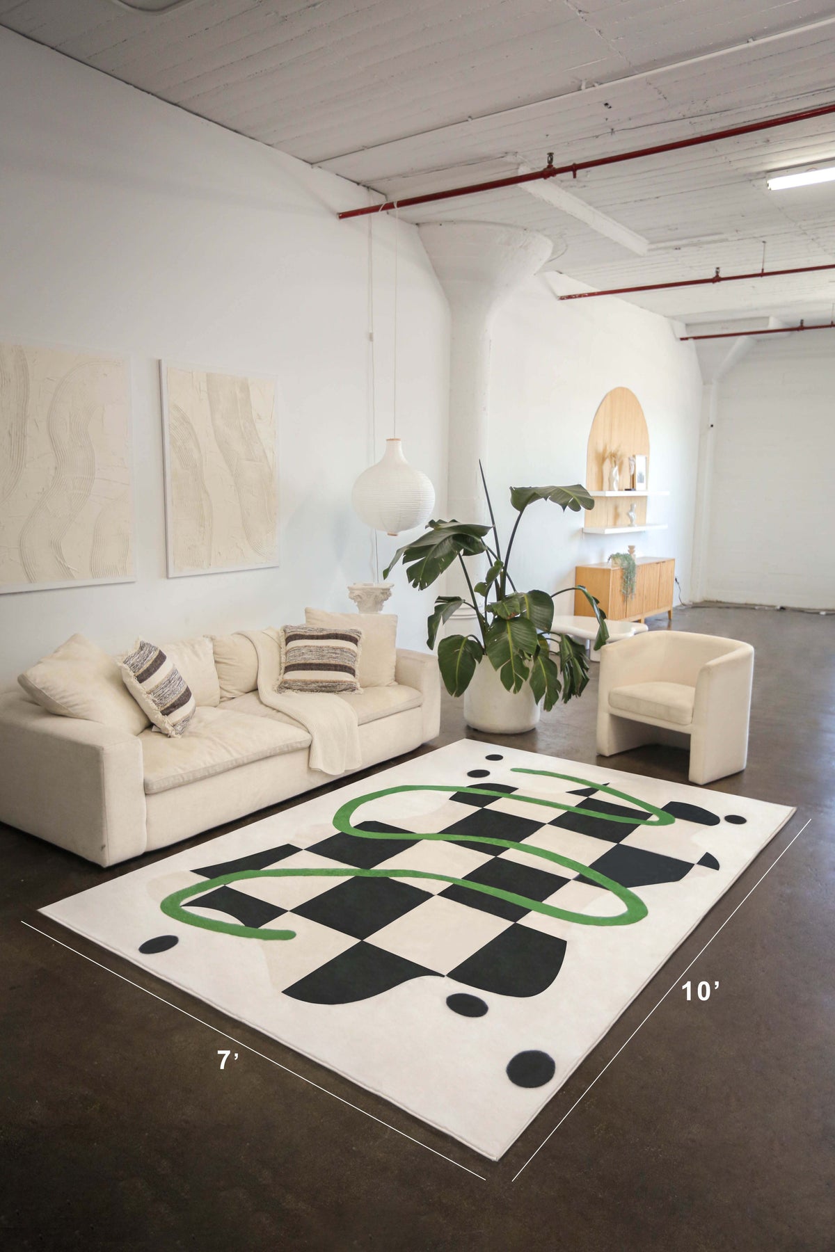 A large 7' x 10' checkered rug with green swirls anchors a neutral-toned living room with sculptural furniture and tall ceilings.