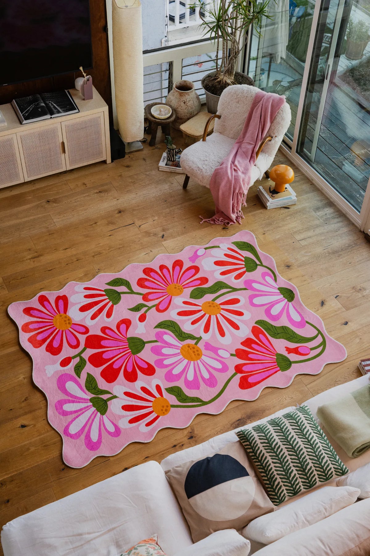 Pink Base Pink Floral Wavy Rug by Jessica Miller placed in a sunlit seating area on wood floor.